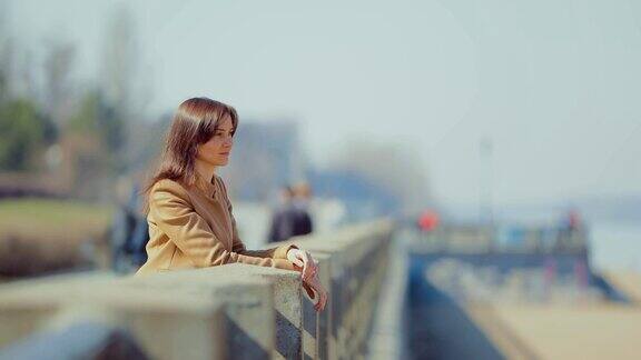 一个漂亮的女孩站在堤岸的栏杆旁向远处望去早春漫步