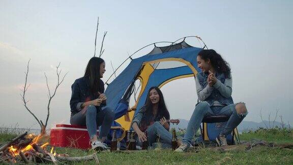 慢镜头一群年轻的亚洲女孩在湖边露营在帐篷前弹吉他一起唱歌露营旅行和友谊