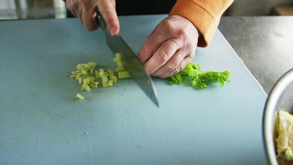 在一家商业厨房里一位年长的白人妇女用菜刀在切菜板上切芹菜