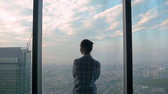 沉思的女人透过摩天大楼的窗户看城市风景