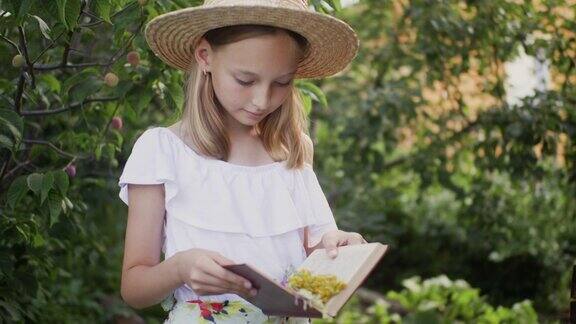 可爱的女孩穿着衣服戴着帽子在夏天的花园里看书
