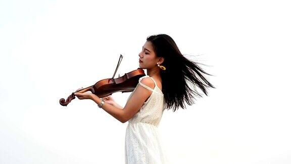 年轻美丽的亚洲女孩穿着裙子在海滩上拉小提琴