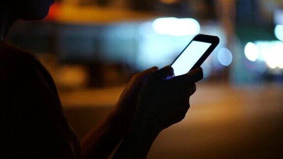 亚洲女性的手正在通过智能手机交流聊天在一个模糊的背景和黑暗的路边夜灯