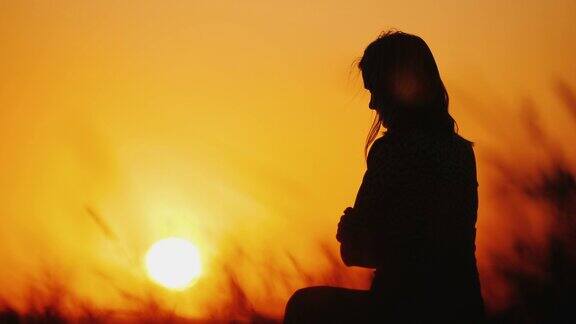 夕阳下一个孤独女人的剪影坐在风中摇曳的草地上