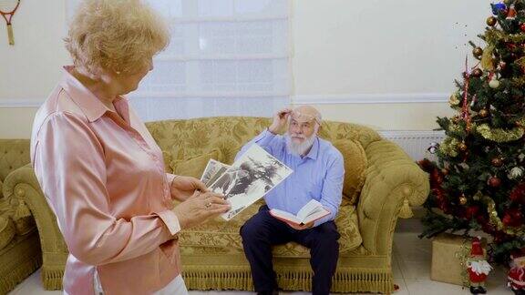 老女人看着她的老照片她的丈夫坐在沙发上看书