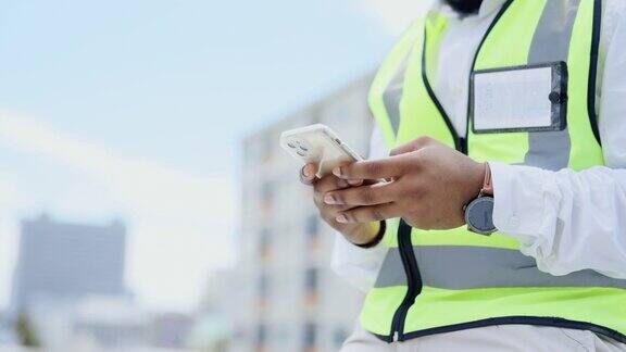 黑人在城市里的手和电话用于建筑规划沟通或社交媒体现场非裔美国男性承包商或工程师在城镇屋顶用智能手机发短信的手