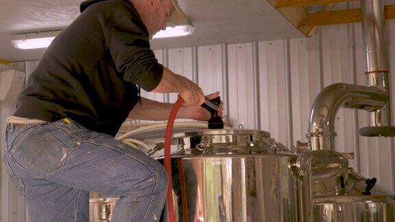一名男性酿酒师正在用软管清洗工艺酿酒厂的发酵罐