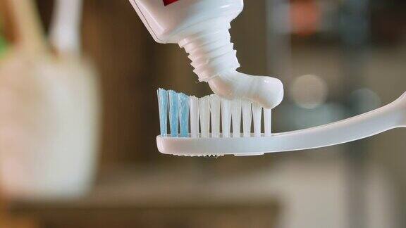 牙膏被涂在白色牙刷上浴室里的散景背景特写清洁牙齿把牙膏从管子里挤出来