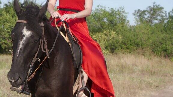 年轻的金发女孩穿着鲜艳的红色长裙骑着黑马