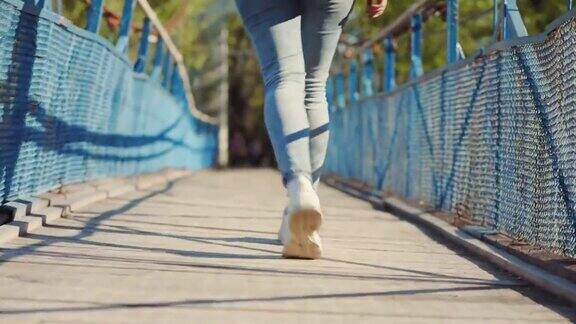 女性的腿在运动鞋是放松的慢慢走在桥上后视图特写
