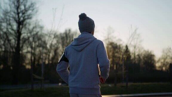 侧视图跟踪慢动作拍摄的运动青年男子在日出时在阳光下跑下公园