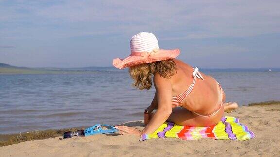 美丽的女人躺在海滩上从她的手中倒沙子