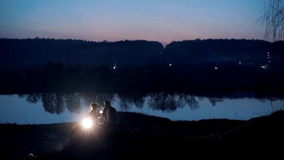 一对年轻美丽的新婚夫妇晚上坐在湖边慢动作
