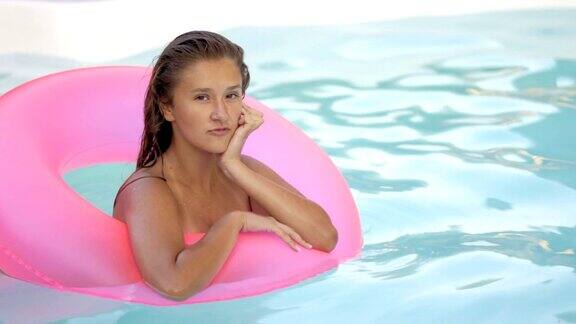 快乐的女孩放松在充气的粉色甜甜圈浮年轻的女人在比基尼享受夏天的假期喝鸡尾酒在粉红色的漂浮在游泳池