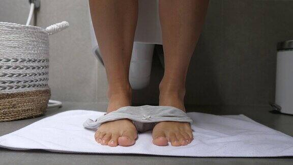厕所里纤细的女性腿特写一名妇女坐在靠墙的马桶上脱下内裤内裤掉到地上的白地毯上