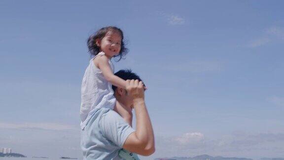亚洲父亲把他的女儿放在他的肩膀上享受在海滩上玩