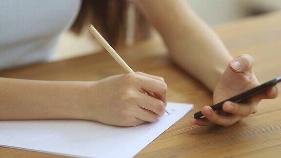 女学生拿着智能手机在纸上做笔记特写