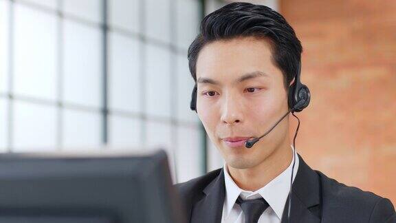 近距离的亚洲人呼叫中心客户服务电话销售穿着正装戴着耳机或耳机在现代办公室与客户交谈