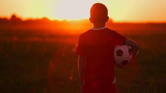 男孩在日落时带着球在田野里男孩梦想成为一名足球运动员男孩在日落时带着球来到田野里