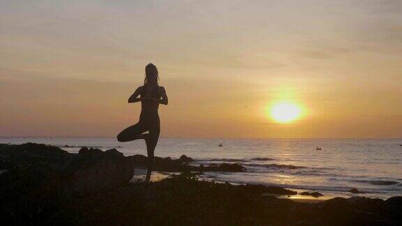 日落时练习剪影瑜伽一个年轻女人在海滩上做瑜伽运动