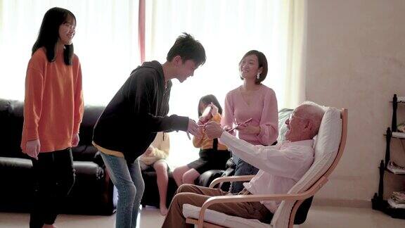 亚洲华人爷爷在家给孙子孙女发红包快乐带着笑脸