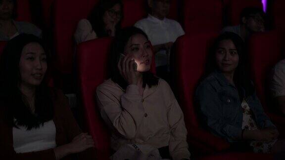 一位亚裔中国年轻女子在电影院看电影时使用智能手机打扰她周围的观众
