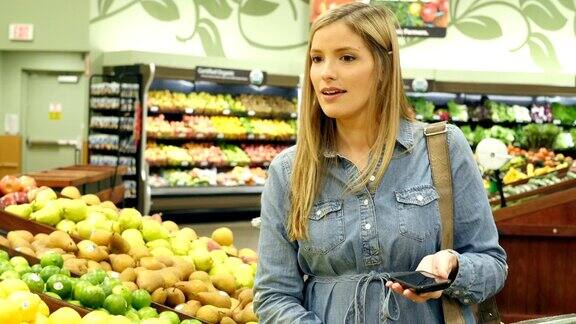 中年白人女性顾客在当地超市的农产品部检查她的智能手机购物清单