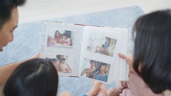亚洲家庭看着旧相册上的照片回忆过去年轻美丽的夫妇与年幼的女儿坐在一起翻阅相册享受回忆关系的记忆