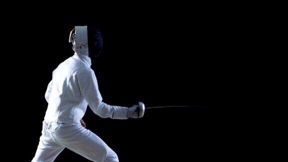 侧面的一个装备齐全的熟练击剑运动员训练他的攻击和刺与陪剑拍摄孤立的黑色背景