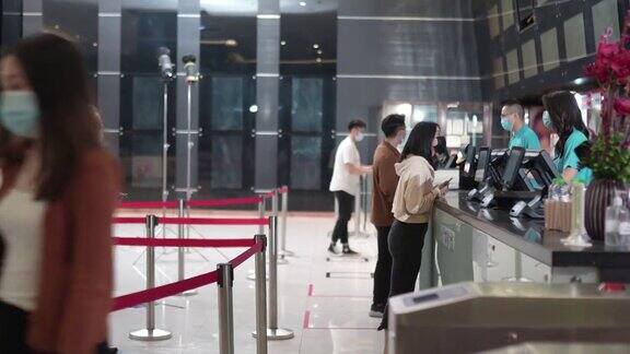 侧视亚洲人群人们戴着口罩排队在电影院买电影票和快餐