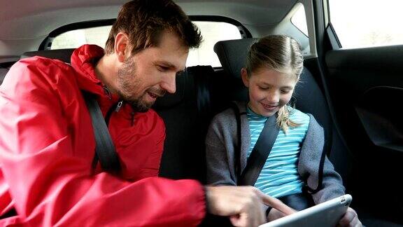 微笑的父亲和女儿用平板电脑坐在车内4K4K