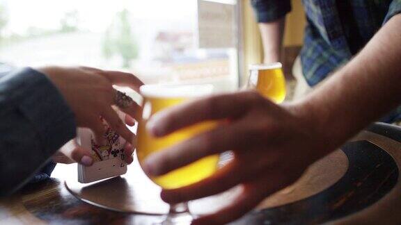 一个白人男人在靠窗的桌子上放下两瓶啤酒而一个年轻女人在洗牌