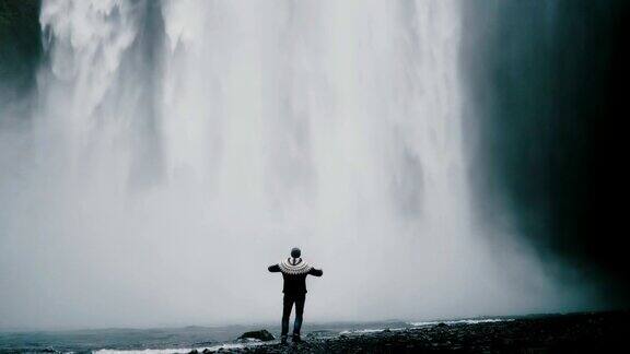 一名年轻的旅游男子走在冰岛强大的Gljufrabui瀑布附近举起双手感到快乐