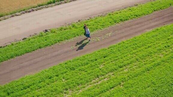 一个年轻的男子和一个女孩在绿色和谷物田旁边的一条土路上慢跑