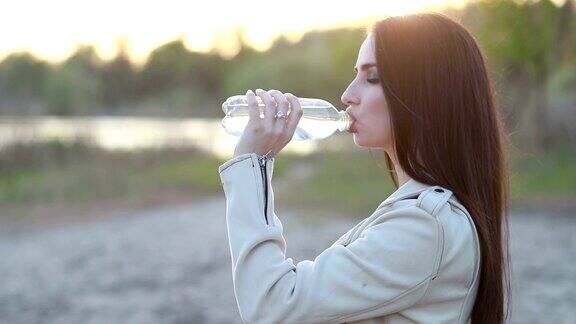 年轻女子在日落时喝水女孩喝瓶子里的水