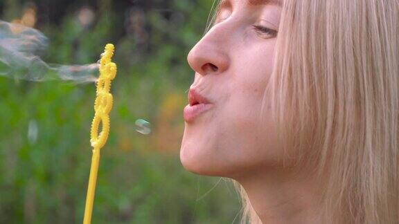 一个年轻的女人在大自然中吹泡泡一个快乐的金发女郎