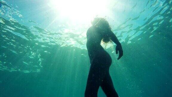 在美丽的太阳耀斑的慢动作中一个女人在水下向着水面游泳