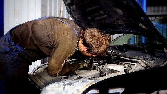 汽车机械师正在发动机罩下修理汽车起动系统