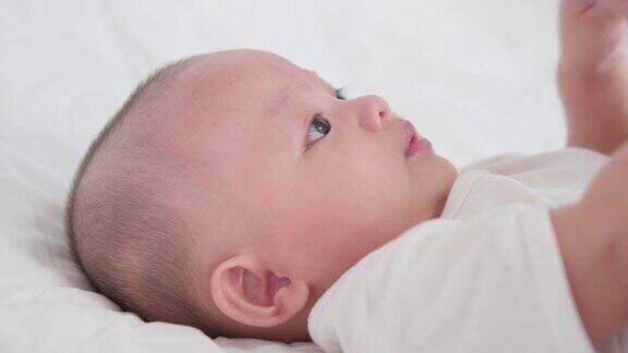特写脸可爱的亚洲新生儿的肖像躺在白色的床上玩看着相机笑着笑着开心的脸天真可爱的小婴儿为人父母和母亲节
