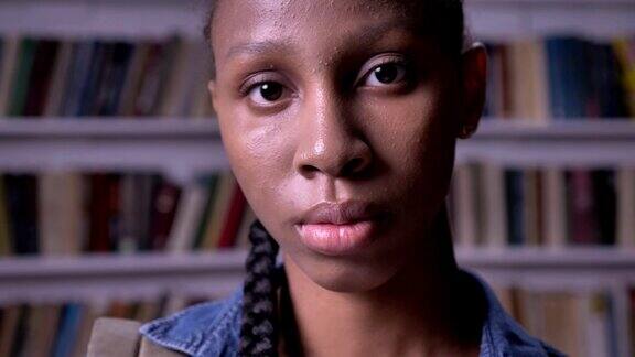 年轻的非裔美国女学生望着镜头站在图书馆里严肃而关切