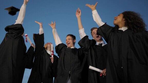 在毕业典礼上一群快乐而兴奋的学生朋友在晚上把他们的帽子抛向空中