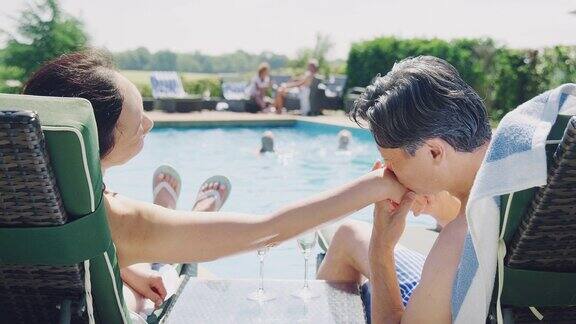 成熟的夫妇在游泳馆边放松在暑假喝香槟
