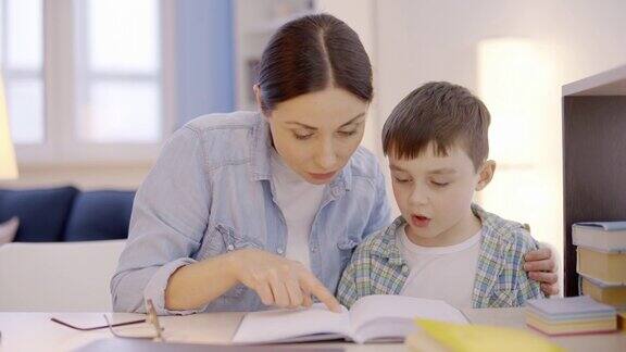 年轻的母亲在家里教儿子阅读帮助做家庭作业诵读困难