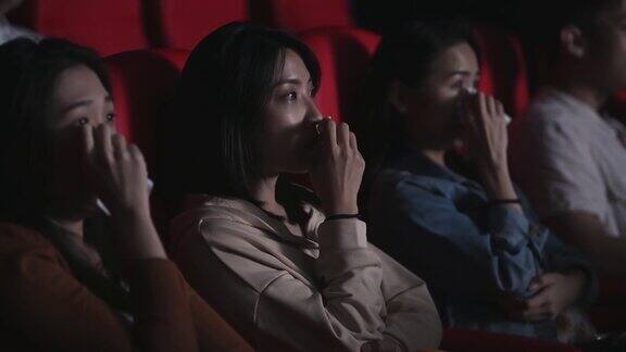 亚洲的中国女人在电影院看感伤的电影在电影院用纸巾擦眼泪
