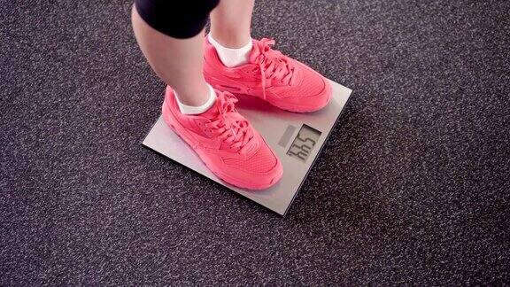 用电子秤秤体重的女孩苗条的女性腿在粉色运动鞋在数字平衡