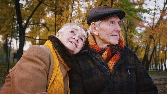 一对幸福的夫妇爷爷奶奶坐在秋天公园的长椅上拥抱着微笑着交谈着
