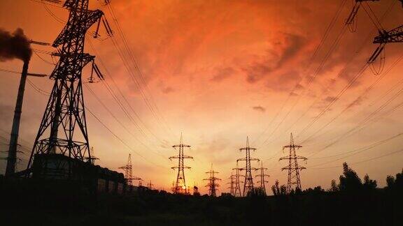 日落时的高压电缆和塔架电力塔的轮廓映衬着戏剧性的天空和红色的夕阳