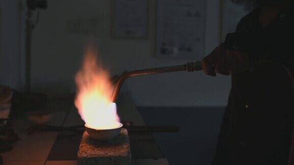 这是亚洲男性金匠珠宝商的手用火把在陶罐中熔化银金属