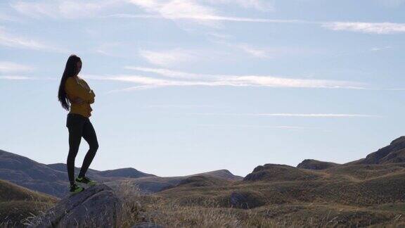 一个骄傲的美丽女孩的剪影在石头上的背景山