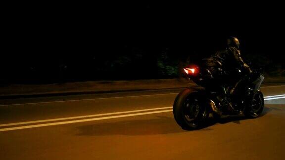 一个戴着头盔的年轻人骑着现代摩托车在夜晚的城市街道上飞驰一个骑摩托车的人在空旷的夜里与他的摩托车赛跑人驾驶自行车自由和爱好侧视图